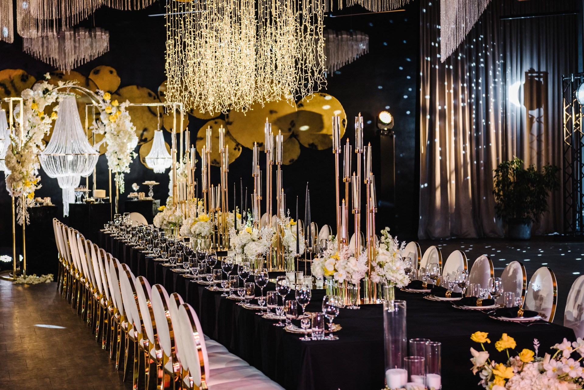 Banquet decoration in hall restaurant. Festive tables with flower composition on black tablecloth and chairs for guests. Wedding set up, dinner table reception in area on party. Setting. Side view.